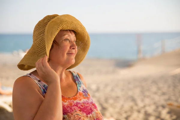 Gülümseyen kıdemli kadın kumsalda şapka — Stok fotoğraf