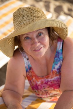 Gülümseyen kıdemli kadın plajda şezlong üzerinde şapka