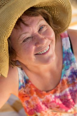 Gülümseyen kıdemli kadın şezlong plajda bir göz ile göz kırpıyor