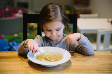 Bir kase makarna çorbası ile küçük bir kız.