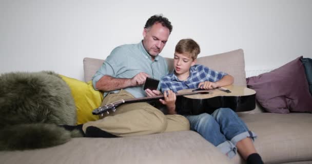 父息子のスマート フォンを使ってギターを再生する方法を教える — ストック動画
