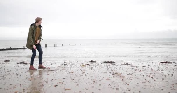 冬天海滩上的年轻男性掠过的石头 — 图库视频影像