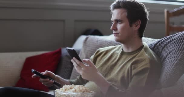 Młody Mężczyzna Pomocą Smartfona Przesyłania Strumieniowego Filmu Domu Jedzenie Popcorn — Wideo stockowe