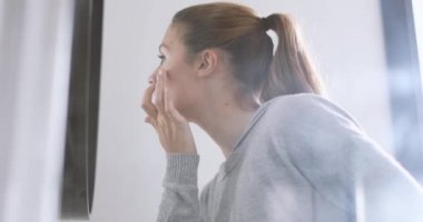 Genç yetişkin kadın cilt inceleyerek aynaya bakıyorum