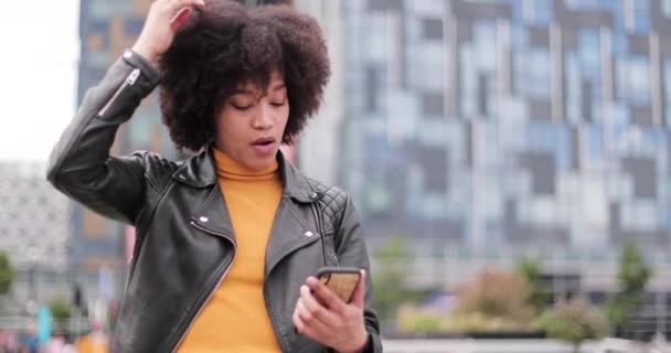 Афроамериканська молода жінка, яка користується смартфоном у місті. — стокове відео