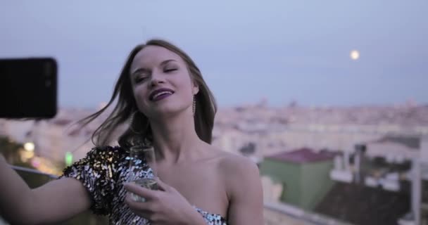 Прелестная кавказка на крыше делает селфи на закате в коктейльном платье — стоковое видео