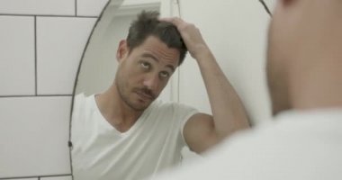 Latin adam banyodaki aynada saçlarını kontrol ediyor.