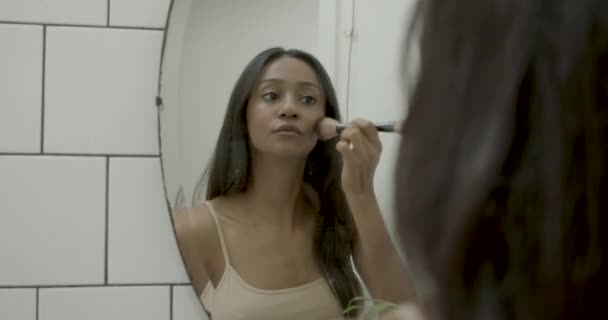 젊은 라틴 여성 이 욕실 거울에 화장을 하고 블루 셔를 사용하는 모습 — 비디오