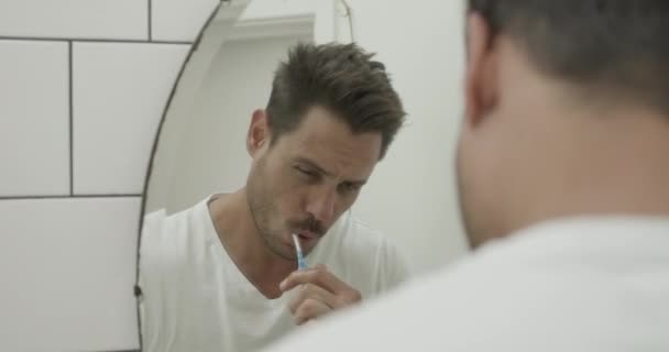 Латинський чоловік чистить зуби і дивиться у дзеркало у ванній — стокове відео