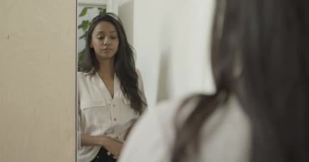 Молодая взрослая латиноамериканка смотрит в зеркало и одевается — стоковое видео