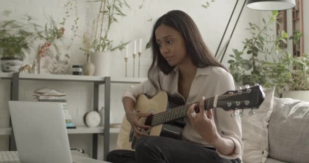 Vuxen kvinna lära sig att spela gitarr på soffan hemma med bärbar dator — Stockvideo