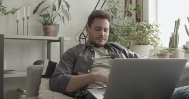 Взрослый мужчина работает из дома на ноутбуке на диване — стоковое видео