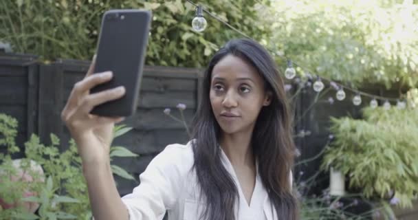 Millennial kvinnliga influencer tar selfie med smart telefon i trädgården på fest på sommaren — Stockvideo