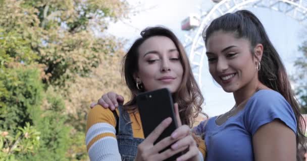 Girlfriends fazer exame de um selfie durante férias de verão com roda gigante no fundo — Vídeo de Stock