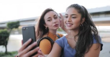 Kız arkadaşlar yazın gün batımında rıhtımda selfie çekerler.