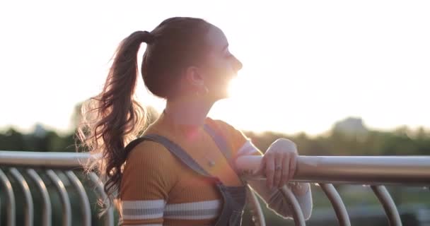Красивая молодая женщина смотрит на мост на закате над набережной — стоковое видео