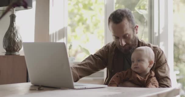 Egyedülálló apa, aki otthon dolgozik a laptopon, és vigyáz a kisfiára. — Stock videók