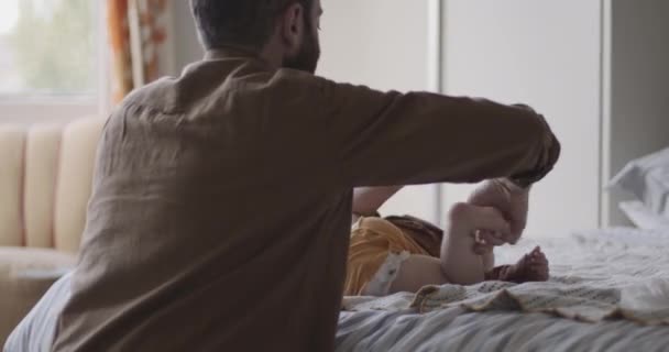 Батько міняє підгузники дитини в спальні — стокове відео