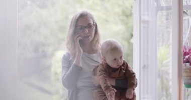 Bekar bir anne akıllı telefonuyla evde çalışıyor ve kucağında bebek var.