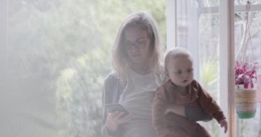Bekar bir anne akıllı telefonuyla evde çalışıyor ve kucağında bebek var.