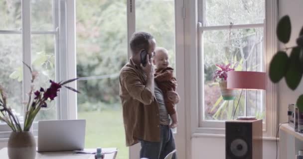 Evde çalışan bekar bir ebeveyn akıllı telefonla ve kucağında bebekle. — Stok video