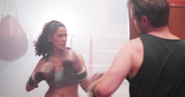 Boxeadora hembra golpeando una bolsa de punzonado con entrenador. — Vídeo de stock
