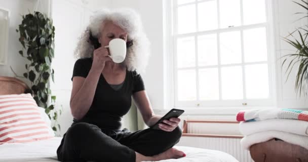 Ηλικιωμένη ενήλικη γυναίκα που κοιτάζει smartphone ενώ έχει πρωινό καφέ — Αρχείο Βίντεο