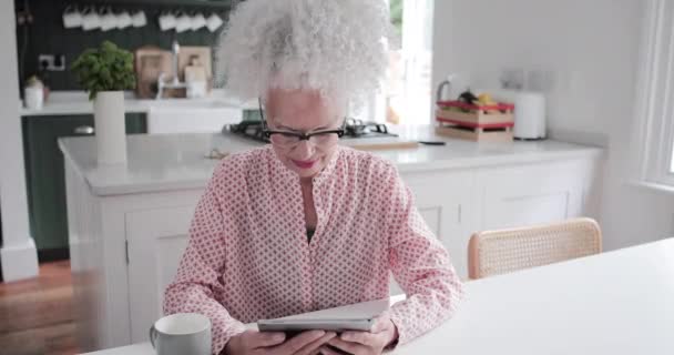 Oudere volwassen vrouw op zoek naar digitale tablet tijdens het drinken van koffie in de ochtend — Stockvideo