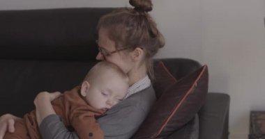 Bekar anne, oturma odasında sandalyeye oturup bebeği rahatlatıyor.