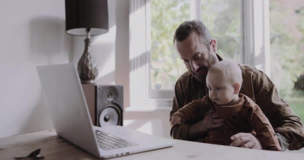 Alleinerziehender Vater arbeitet von zu Hause aus am Laptop und kümmert sich um kleinen Sohn — Stockvideo