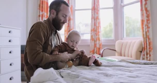 Одинокий батько одягається дитини на ліжко в спальні — стокове відео