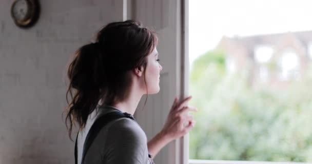 Jeune femme adulte regardant par la fenêtre d'une nouvelle maison — Video