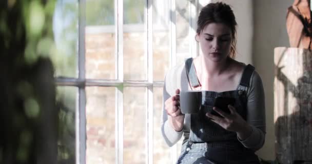 Joven adulta que toma café por la mañana y revisa el teléfono inteligente — Vídeo de stock