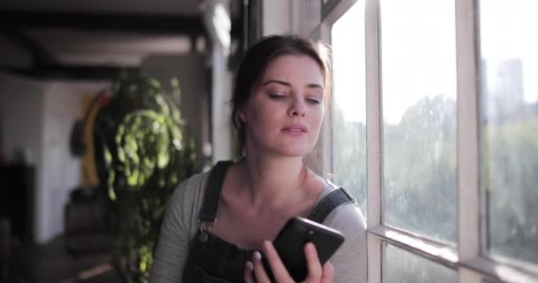 Genç bir kadın sabah güneşinde akıllı telefonu kontrol ediyor. — Stok video