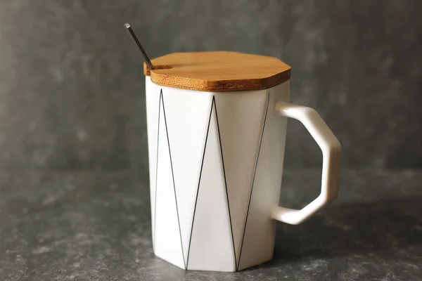 A cup with a lid and a spoon. White cup on a dark background
