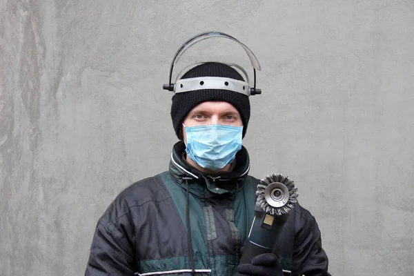 Masked man with grinder in hands. Worker in dirty clothes