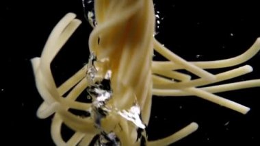 Makarna girdabı, siyah arka planda köpüklerle kaynayan suda dönen spagetti. Yavaş çekim