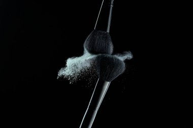 Siyah arka planda renkli barut patlaması olan makyaj fırçaları. Kozmetik ürünlerinin yüksek hız fotoğrafçılığı.