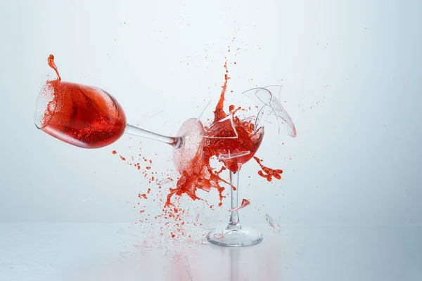 Kırmızı şarap kadehleri uçuyor, çarpışıyor ve beyaz arka planda eziliyor. Sıçramalar. Kırık cam. Sıvıların yüksek hız fotoğrafçılığı