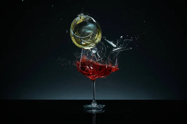 Kırmızı ve beyaz şarap kadehleri uçuşuyor, çarpışıyor ve siyah arka planda eziliyor. Sıçramalar. Kırık cam. Sıvıların yüksek hız fotoğrafçılığı
