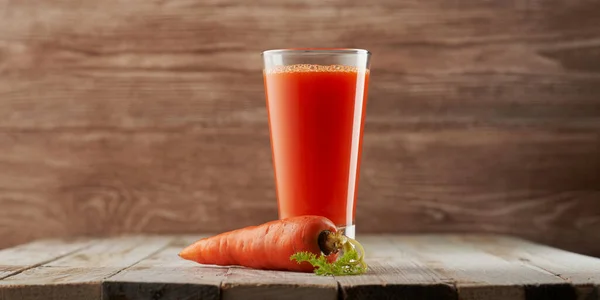 Ahşap arka planda yüksek bardakta taze sıkılmış havuç suyu. Plastik sahne, taze meyve suyu.