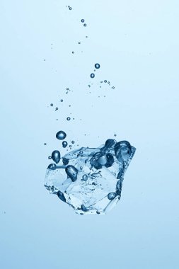 Baloncuklarla suya düşen buz parçası. Soğuk su, buz küpü, buz yığını. Açık mavi arkaplan. Yüksek hız fotoğrafçılığı       