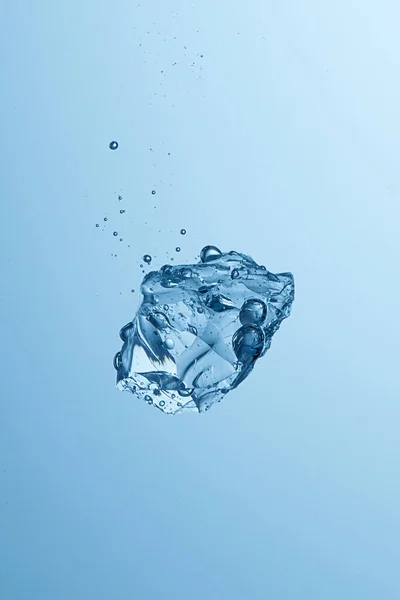Baloncuklarla suya düşen buz parçası. Soğuk su, buz küpü, buz yığını. Açık mavi arkaplan. Yüksek hız fotoğrafçılığı