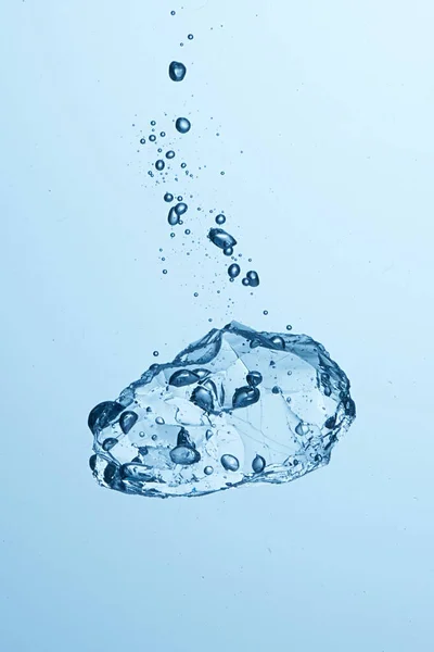 Baloncuklarla suya düşen buz parçası. Soğuk su, buz küpü, buz yığını. Açık mavi arkaplan. Yüksek hız fotoğrafçılığı
