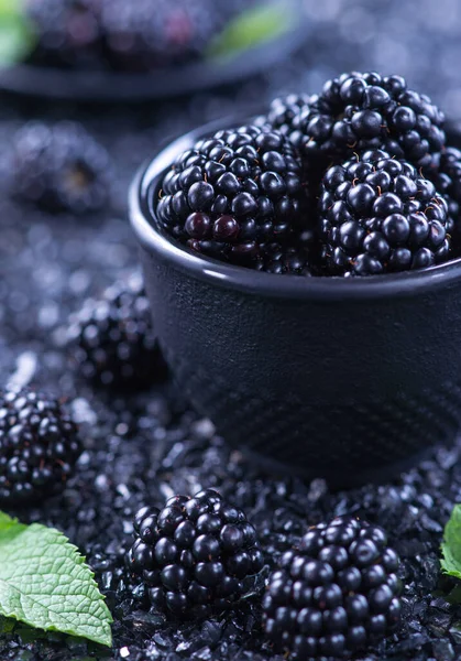 Siyah parlak arka planda siyah bir kasede bir sürü böğürtlen. Büyük taze meyveler.