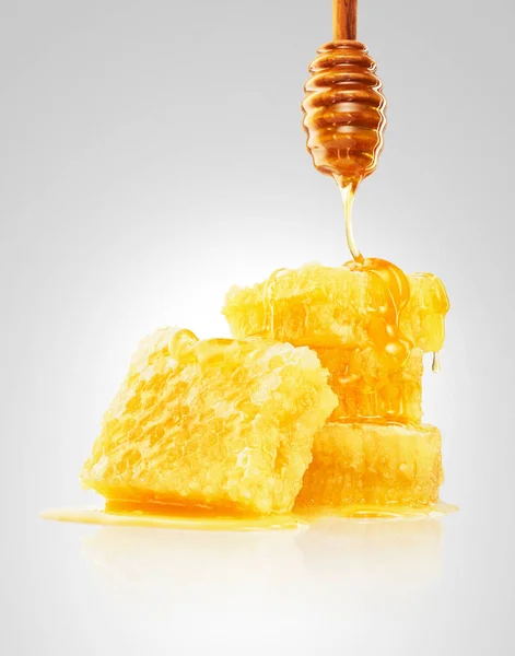 Altın bal, açık gri arka planda izole edilmiş ahşap kaplamalı bal peteğine dökülüyor. Akan bal                