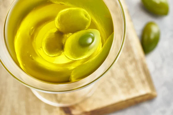 Martini bardağında yeşil zeytin ve zeytin yağı. Tahta tahta, açık gri arka plan. Üst görünüm