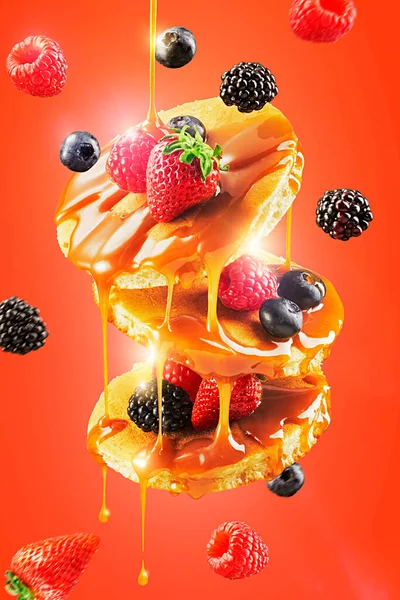 Altın şurupla kaplı uçan Amerikan gözlemeleri. Uçan dutlar - böğürtlen, ahududu, yabanmersini, çilek. Kırmızı arka plan. Yiyecek havalanması 