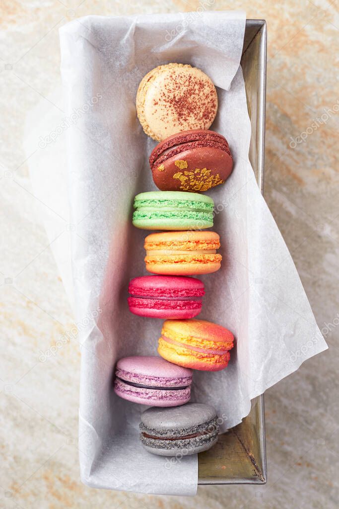 Colorful macaroons in a metal tray on marble surface, top view