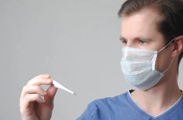 Een Man Met Een Medisch Masker Kijkt Naar Een Thermometer — Stockfoto